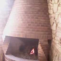 Murowany kominek z cegły, z palącym się ogniem, w pomieszczeniu z kamiennymi ścianami.