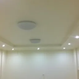 Pomalowane na kremowo wnętrze z dwiema okrągłymi lampami sufitowymi i rzędem punktowych reflektorów LED wzdłuż krawędzi sufitu podwieszanego.