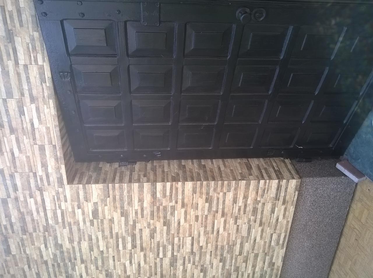 Fragment ściany wykończonej mozaiką z płytek imitujących kamień, z widoczną górną krawędzią pomalowanej na czarno konstrukcji, prawdopodobnie drzwi lub bramy.