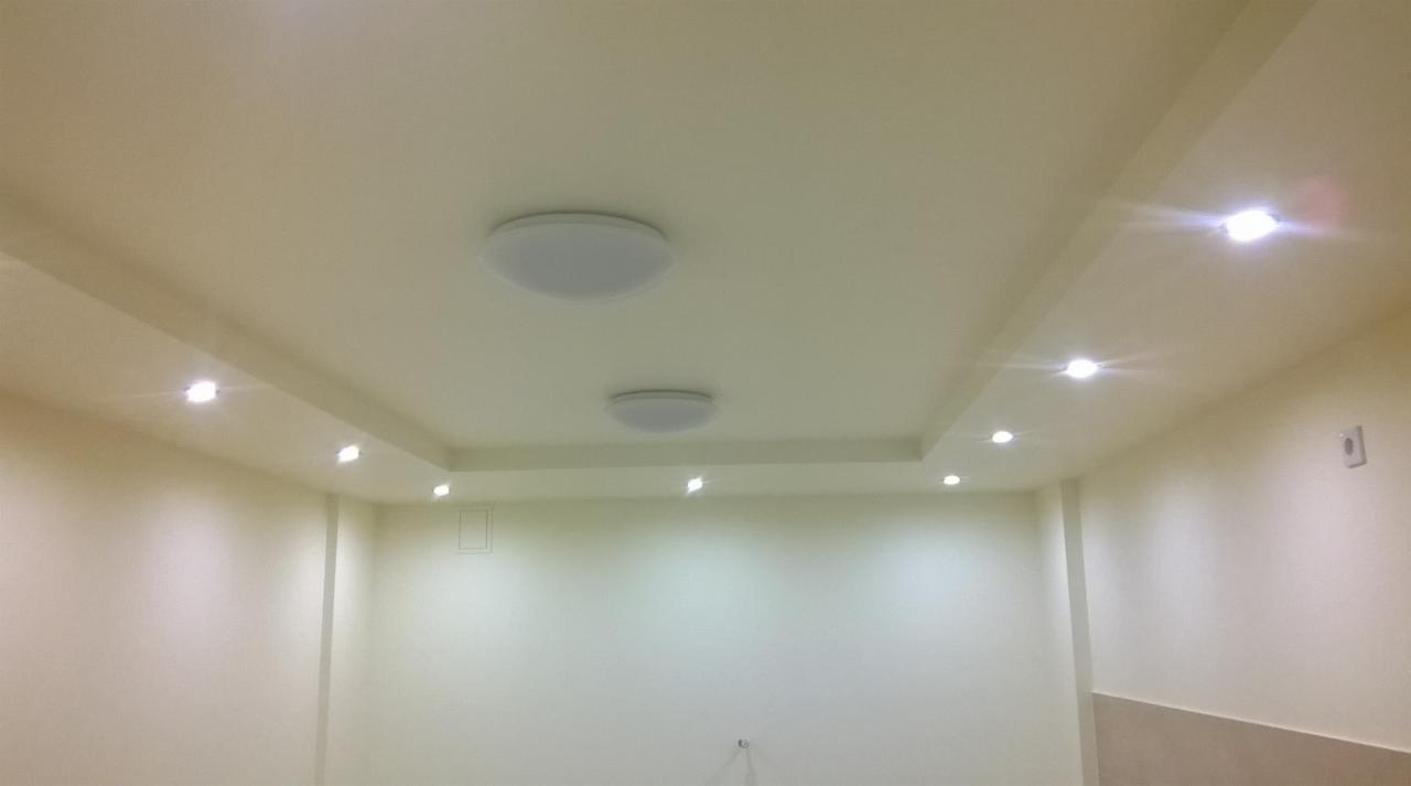 Pomalowane na kremowo wnętrze z dwiema okrągłymi lampami sufitowymi i rzędem punktowych reflektorów LED wzdłuż krawędzi sufitu podwieszanego.