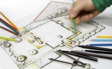 Ręka rysuje zielonym ołówkiem odręczny plan zagospodarowania terenu z elementami ogrodu, widoczne kolorowe kredki, cyrkiel i linijka.