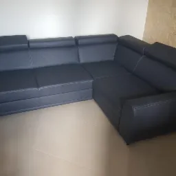 Ciemnogranatowy narożnik z regulowanymi zagłówkami i jasnymi przeszyciami, ustawiony na beżowej podłodze na tle ściany z dekoracyjną okładziną.