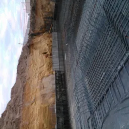 Wykonany wykop pod fundament z widoczną ścianą ziemi, deskowaniem oraz siatką zbrojeniową ułożoną na folii.