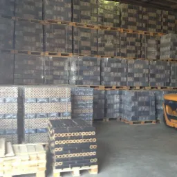 Magazyn z ułożonymi na paletach brykietami PINI KAY, część zafoliowana, w tle wózek widłowy.