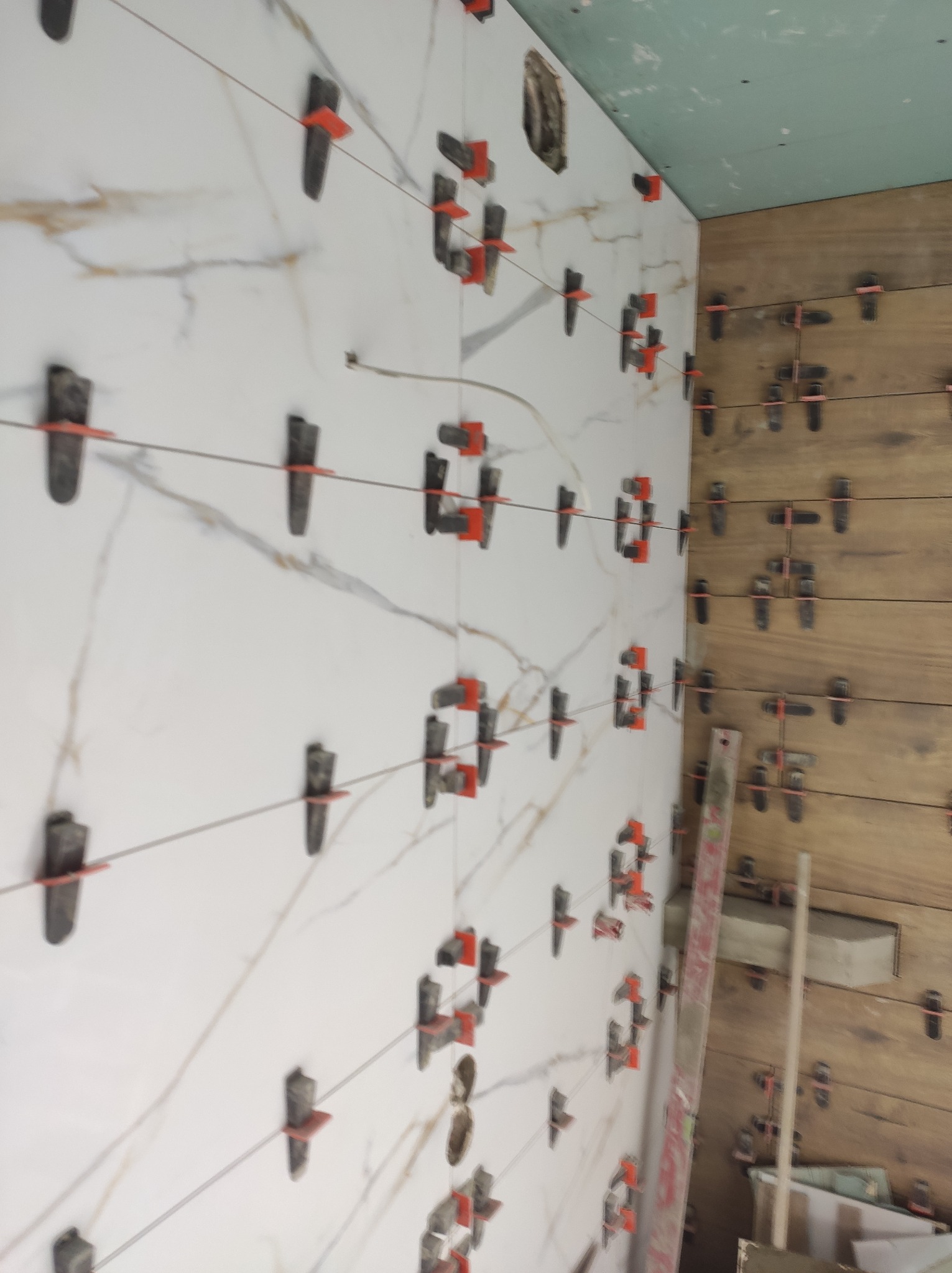 Układanie płytek imitujących marmur i drewno z użyciem systemu poziomowania płytek, widok na ścianę w Byczynie.