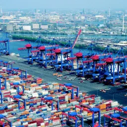 Panorama portu w Skierniewicach z licznymi kontenerami i dźwigami w kolorach niebieskim i czerwonym, w tle widok na miasto.