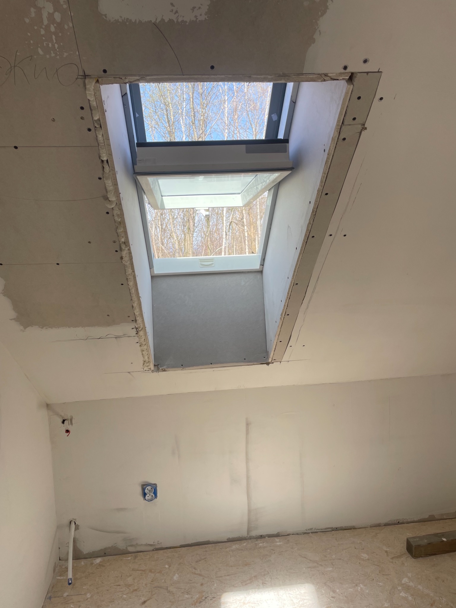 Montaż okna dachowego w otworze wykończonym płytą karton gips, widoczne łączenia płyt wymagające szpachlowania, instalacja elektryczna w ścianie.