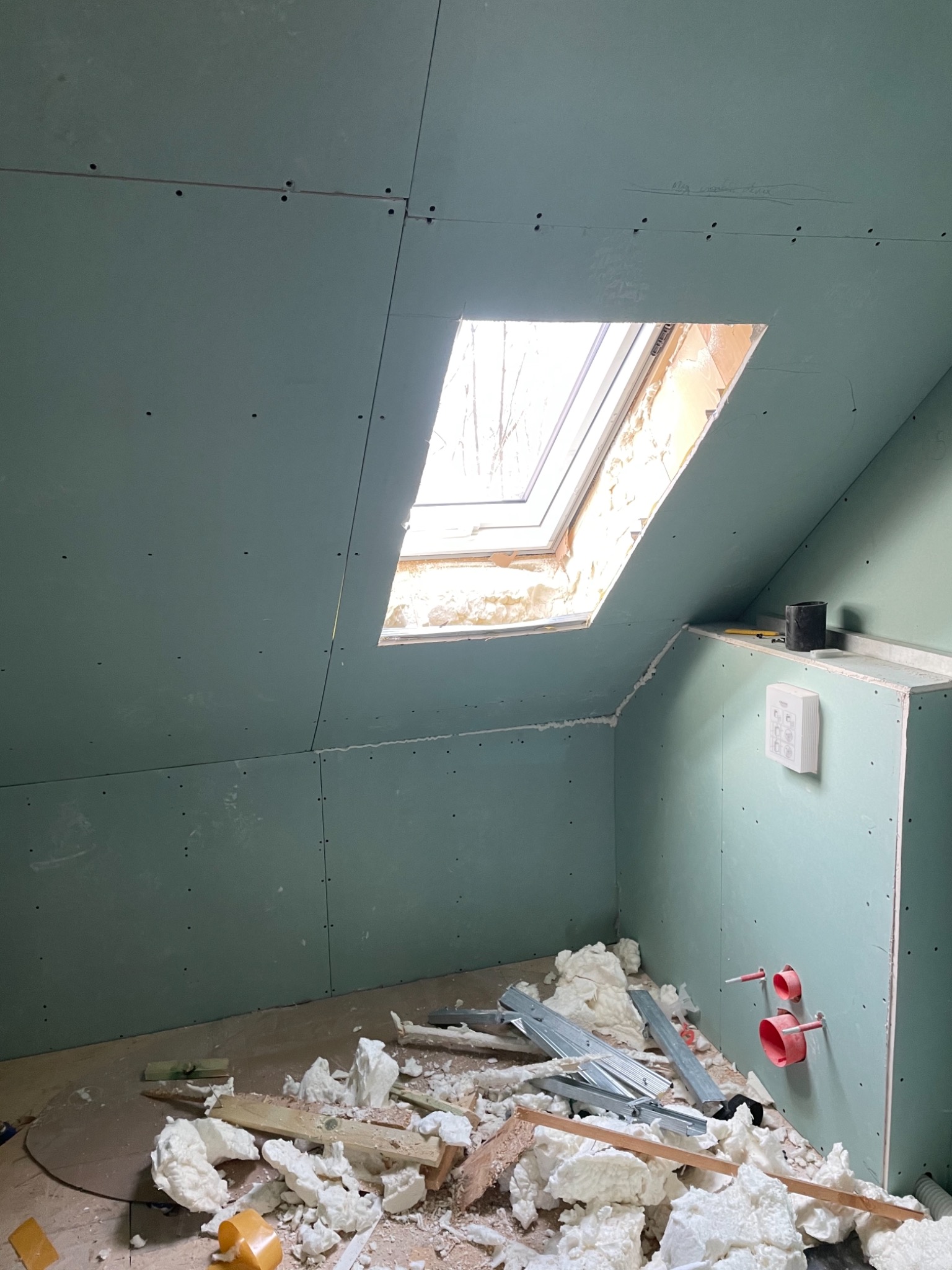 Montaż ścian działowych z płyty gipsowo-kartonowej w poddaszu w Jeleniej Górze, widoczne okno dachowe i instalacja sanitarna, pozostałości po montażu na podłodze.