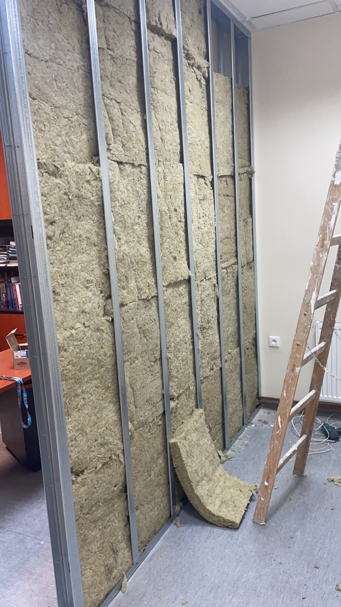 Konstrukcja metalowa ściany z wypełnieniem z wełny mineralnej, widoczna drabina i fragment pomieszczenia w trakcie prac wykończeniowych.