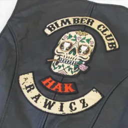 Czarna skórzana kamizelka motocyklowa z naszywkami: czaszka z kwiatami i różą w ustach, napis 'Bimber Club' oraz 'Arawicz Hak'.