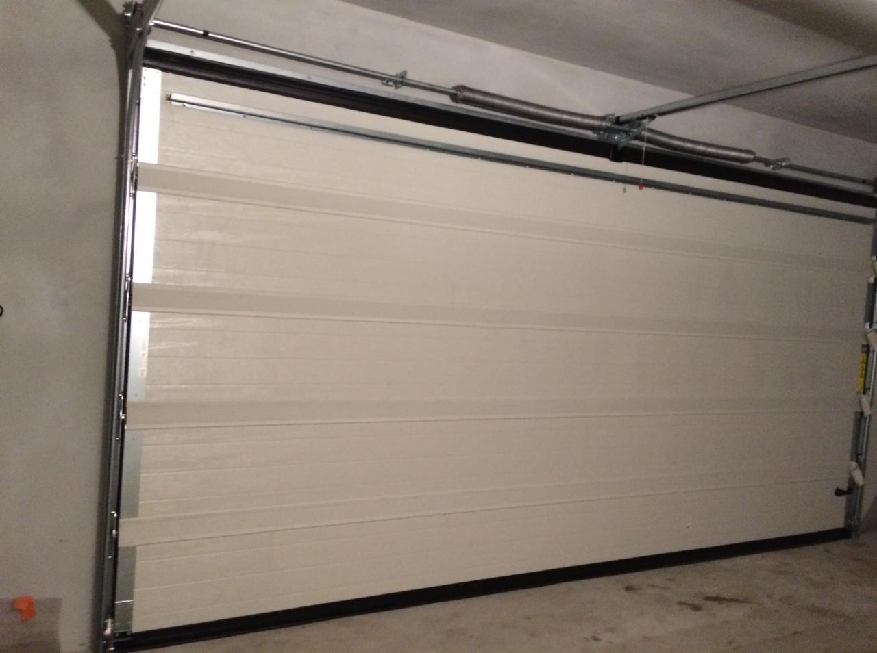 Zamknięta, segmentowa brama garażowa w kolorze kremowym, widoczne sprężyny i mechanizm mocujący do sufitu.