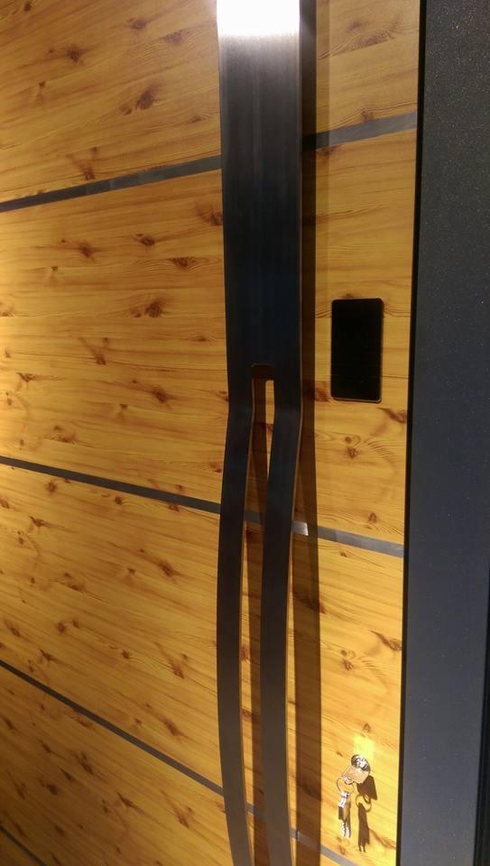 Drewniane drzwi z metalowym, podłużnym uchwytem i poziomymi wstawkami, widoczne klucze w zamku.