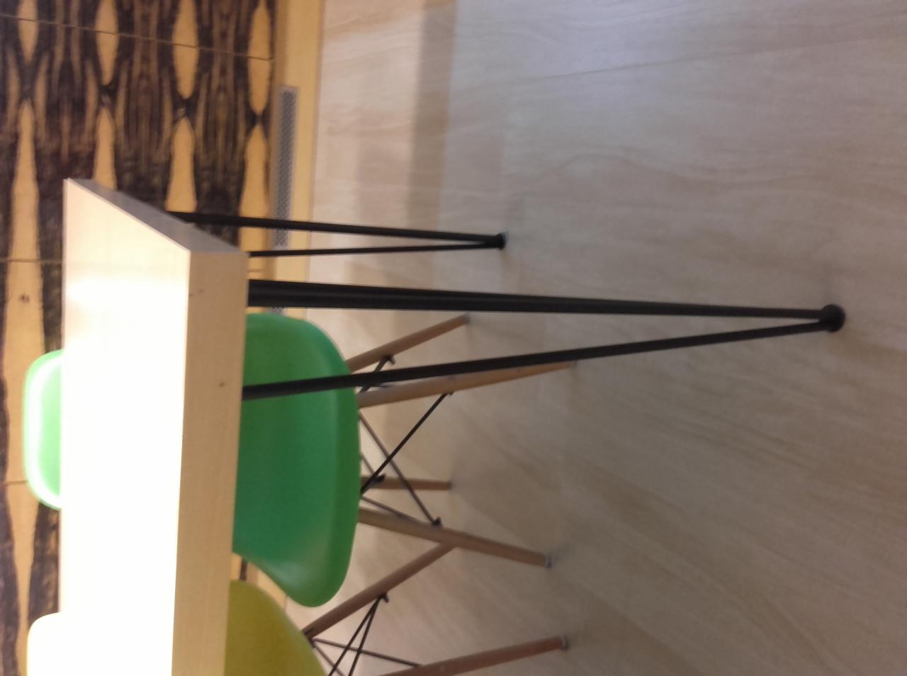 Metalowe nogi stołu z krzesłami z tworzywa sztucznego w tle, widoczne elementy konstrukcyjne.