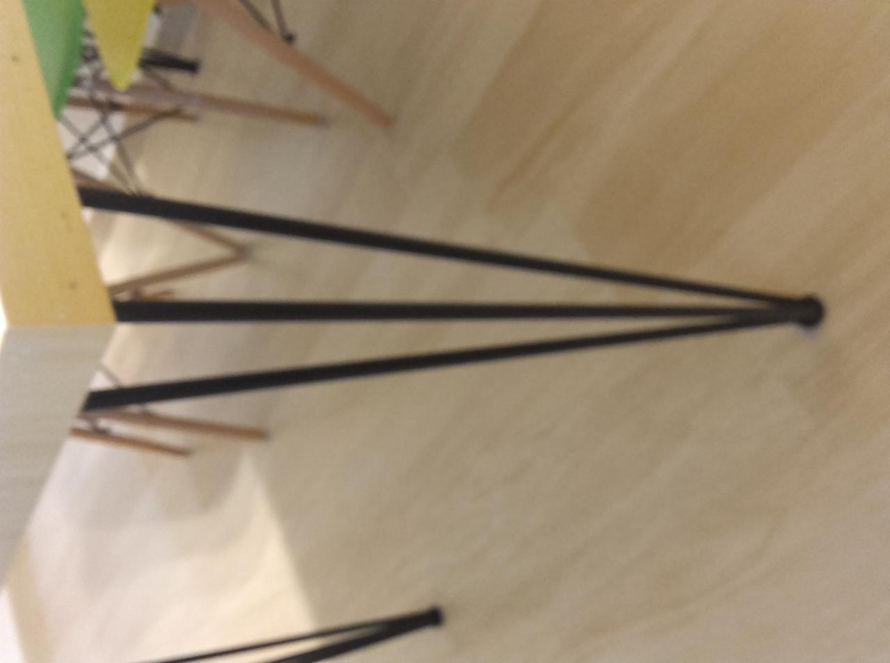 Czarna metalowa podstawa stołu z trzema nogami, widok z dołu, na jasnej drewnianej podłodze.