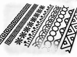 Czarne, metalowe listwy dekoracyjne o różnych wzorach geometrycznych, ułożone ukośnie na białym tle.