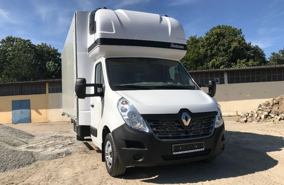 Biały samochód dostawczy Renault Master z wysoką zabudową kontenerową, zaparkowany na placu z materiałami budowlanymi, widok z przodu.