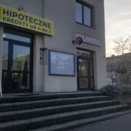 Wejście do placówki oferującej kredyty hipoteczne i dla firm, z widocznym szyldem i banerem reklamowym na zewnątrz budynku.