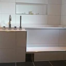 JLInwesting - Nowoczesna łazienka z wanną obudowaną białymi płytkami, bateria umywalkowa czterootworowa na blacie i czarne płytki podłogowe.