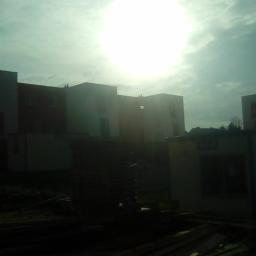 JLInwesting - Surowy stan budowy wielorodzinnego domu z widocznym placem budowy i stertami materiałów w słoneczny dzień.