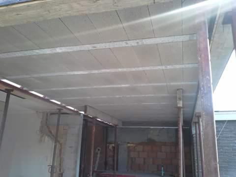 Wnętrze w trakcie budowy z widocznym stropem żelbetowym podpartym metalowymi stemplami, ściany częściowo wymurowane z cegły, surowy stan wykończenia.