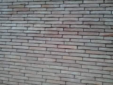 Fragment ściany z jasnoszarej cegły klinkierowej, ułożonej w regularny wzór z poziomymi spoinami, widoczne lekkie zabrudzenia na niektórych cegłach.