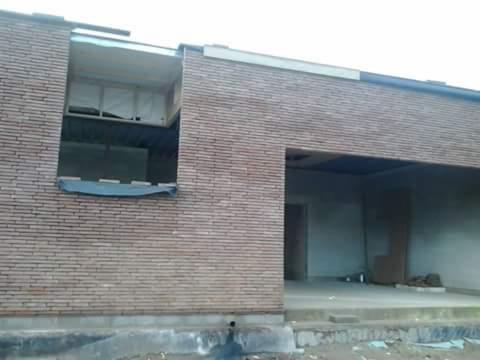 Surowy stan murowanego budynku z widocznym oknem zabezpieczonym folią i otwartym przejściem, ukazujący etap budowy przed wykończeniem elewacji.