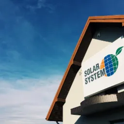 Budynek z logo firmy Solar System przedstawiającym glob z liściem, na tle błękitnego nieba.