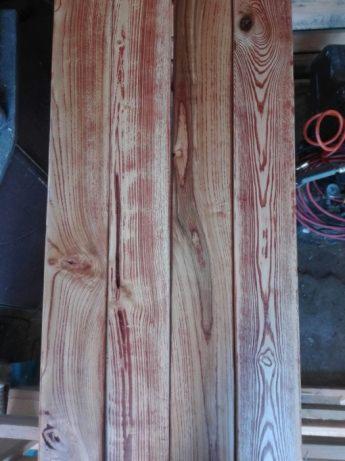 Cztery deski parkietowe z wyraźnym usłojeniem i czerwonym zabarwieniem, leżące obok narzędzi w warsztacie.