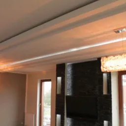 Salon z dekoracyjnym sufitem podwieszanym, kamienną ścianą z wnękami oświetleniowymi i dwoma różnymi lampami wiszącymi.