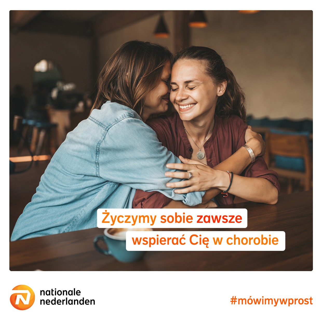 Dwie uśmiechnięte kobiety obejmujące się przy stole z filiżanką kawy, slogan 'Życzymy sobie zawsze wspierać Cię w chorobie' oraz logo Nationale Nederlanden.