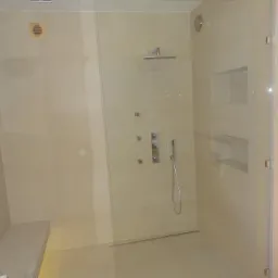 Nowoczesna kabina prysznicowa z deszczownicą, wykończona beżowymi płytkami, z wbudowanymi półkami i siedziskiem z mozaiki.