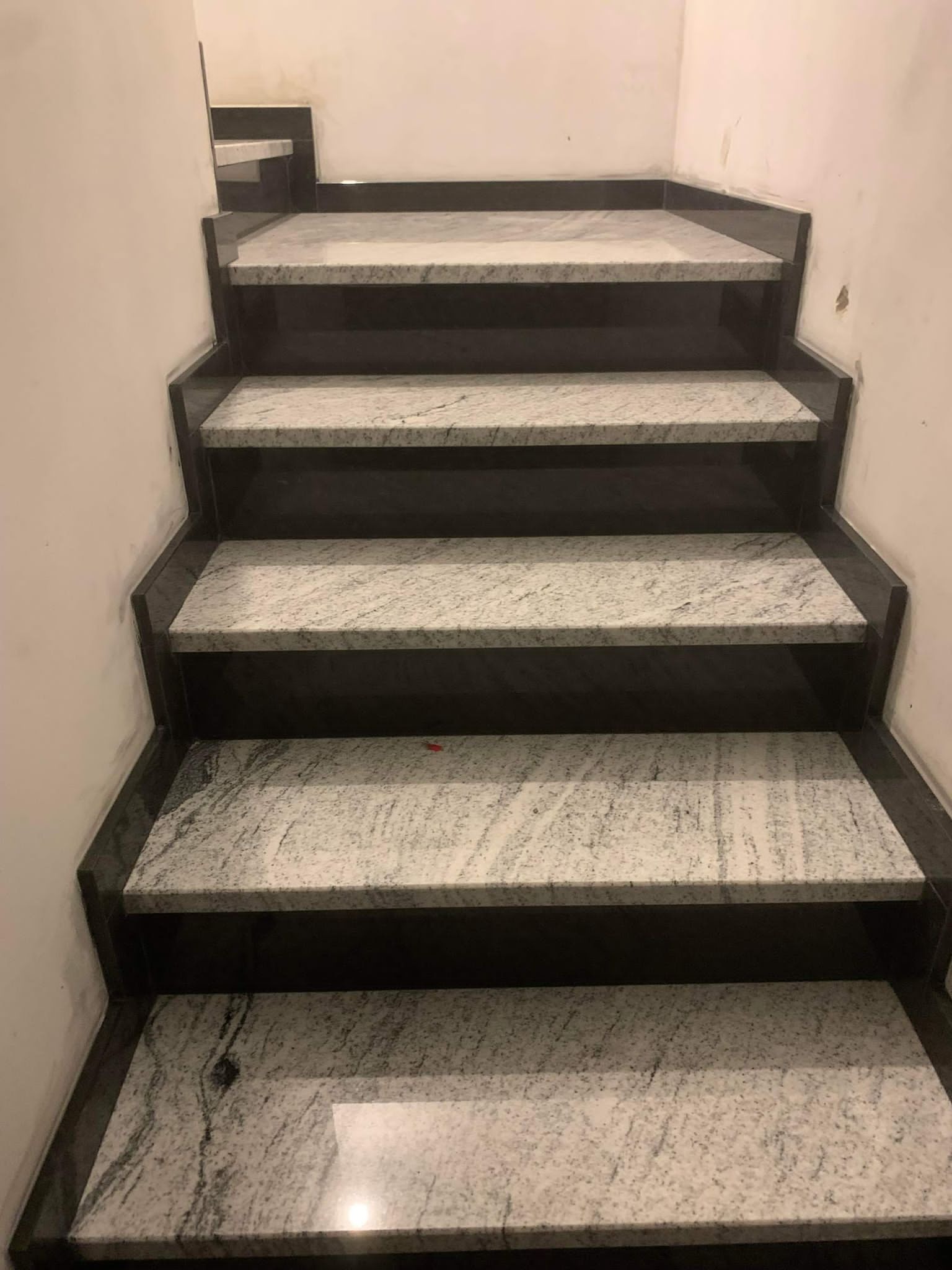 Wewnętrzne schody z szarego kamienia z ciemnymi podstopnicami, widok z dołu na górę, ściana w tle.