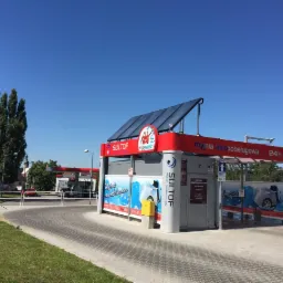 Zewnętrzny widok samoobsługowej myjni samochodowej SULTOF z panelami fotowoltaicznymi na dachu, zlokalizowanej w pobliżu stacji benzynowej Orlen, w słoneczny dzień.