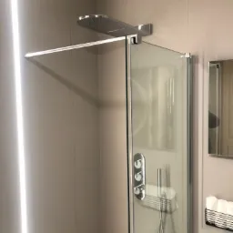 Nowoczesna kabina prysznicowa z deszczownicą i szklanymi drzwiami, widoczne sterowanie temperaturą i półka z ręcznikami wewnątrz, minimalistyczny design łazienki w odcieniach beżu.