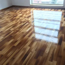 Błyszcząca, świeżo wycyklinowana podłoga parkietowa z wyraźnym odbiciem okna, ukazująca efekt gładkiej powierzchni i odnowionego drewna.