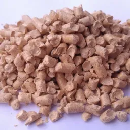 Góra jasnobrązowych, cylindrycznych brykietów z trocin na białym tle, widoczne drobne pęknięcia i nierówności na powierzchni pelletu.