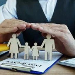 Ochronne dłonie nad drewnianą rodzinką na formularzu ubezpieczeniowym w Zgierzu, symbolizujące bezpieczeństwo finansowe.