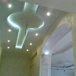 Wykończony sufit podwieszany z oświetleniem punktowym i centralnym elementem dekoracyjnym w kształcie krzyża z podświetleniem LED, widoczny łuk z dekoracyjnym filarem i teksturowane ściany...