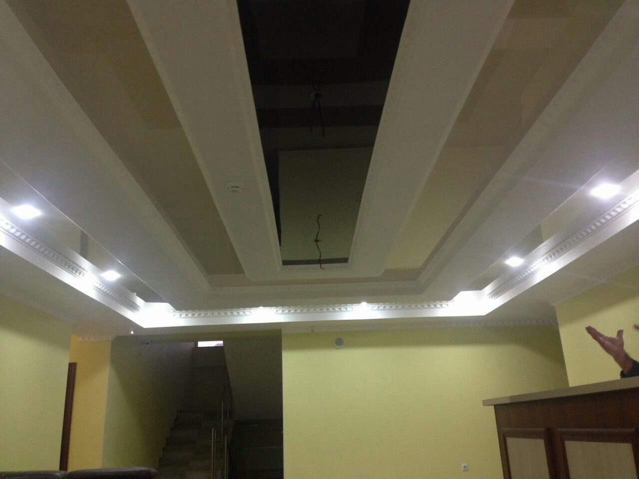 Wykończony sufit podwieszany z oświetleniem punktowym i dekoracyjnymi listwami w pomieszczeniu z żółtymi ścianami i widocznym wejściem na schody.