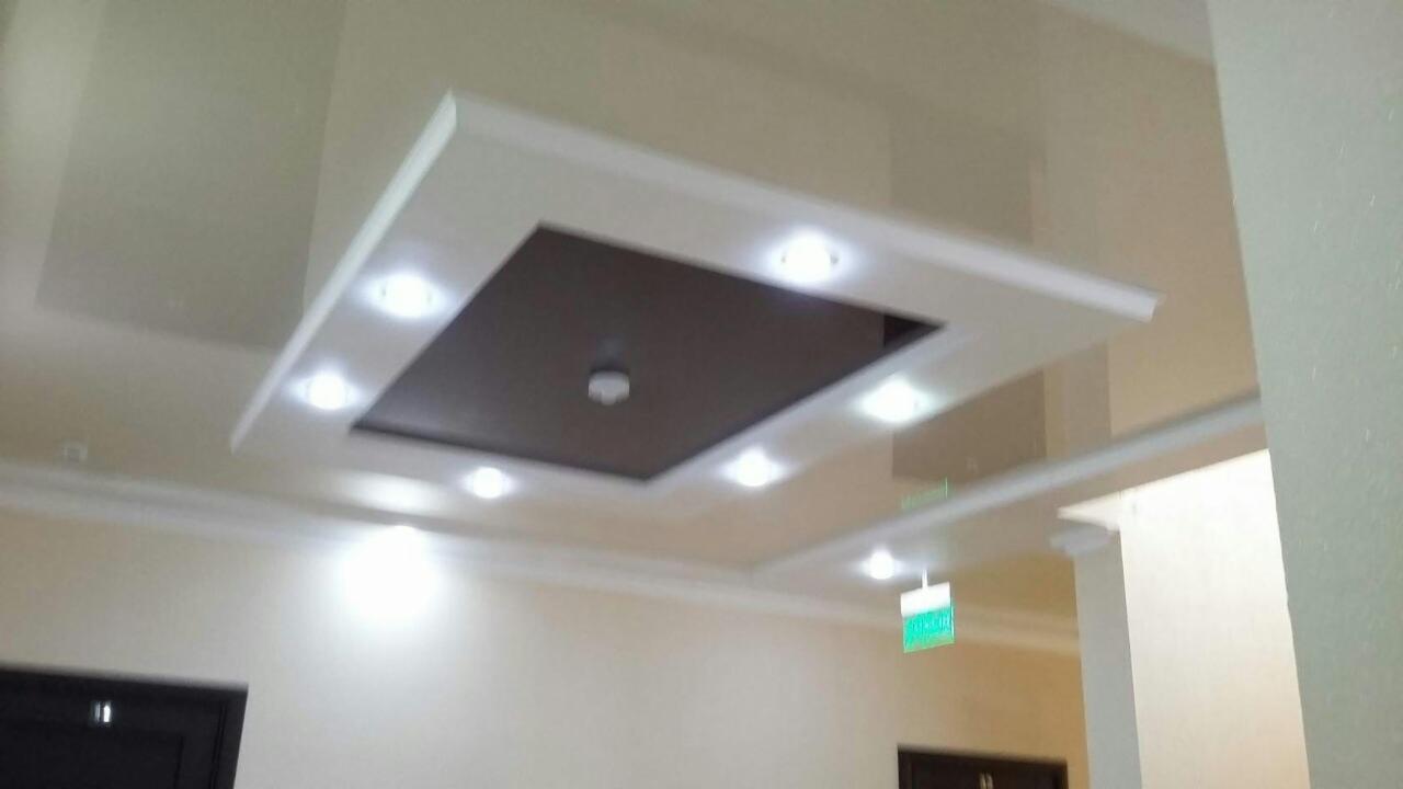 Wykończony sufit podwieszany z oświetleniem punktowym, brązowy panel centralny i biała rama, widok z dołu w jasnym wnętrzu.