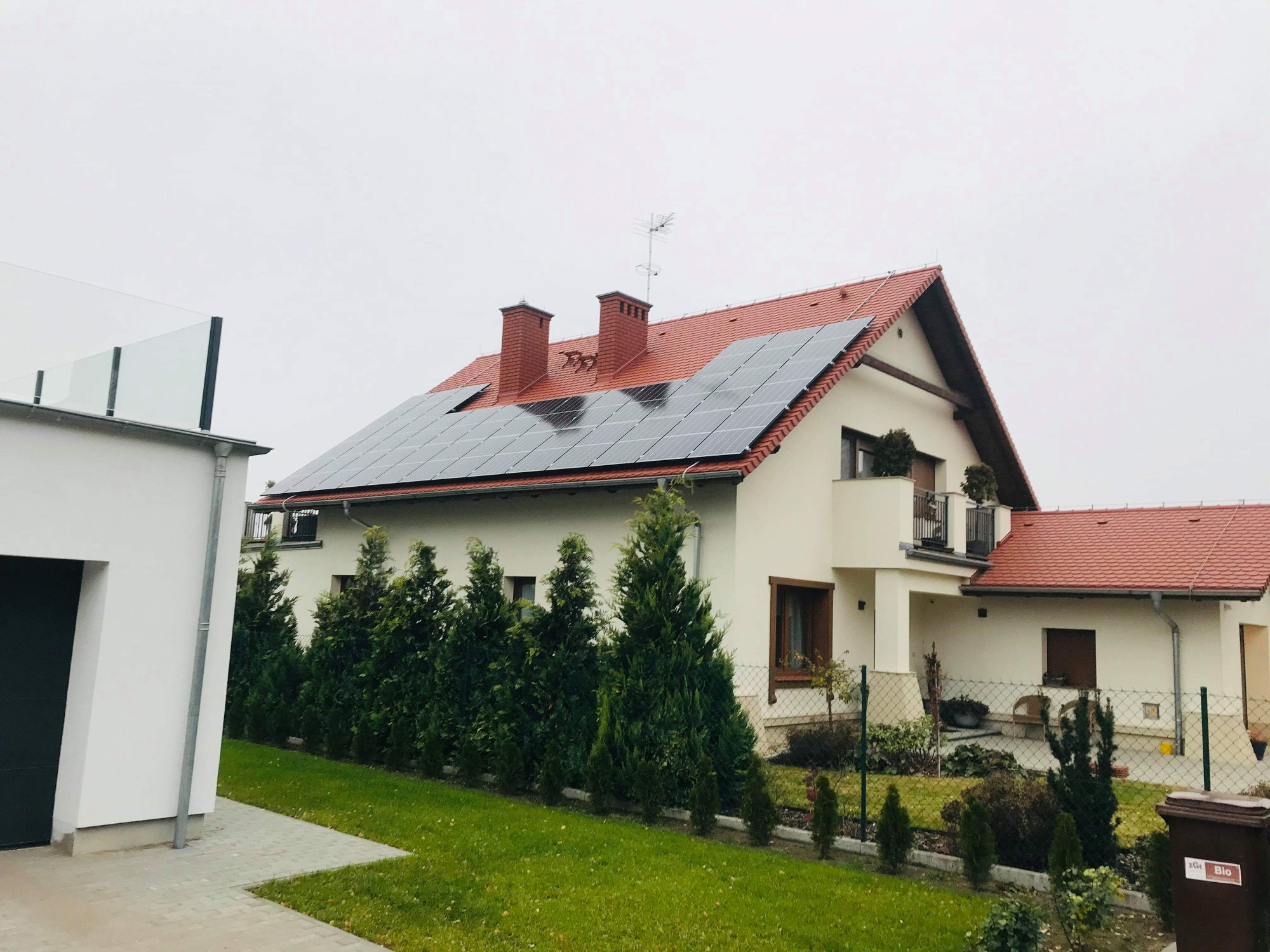 Dom jednorodzinny z czerwonym dachem i panelami słonecznymi na dachu, widok z poziomu gruntu w pochmurny dzień.