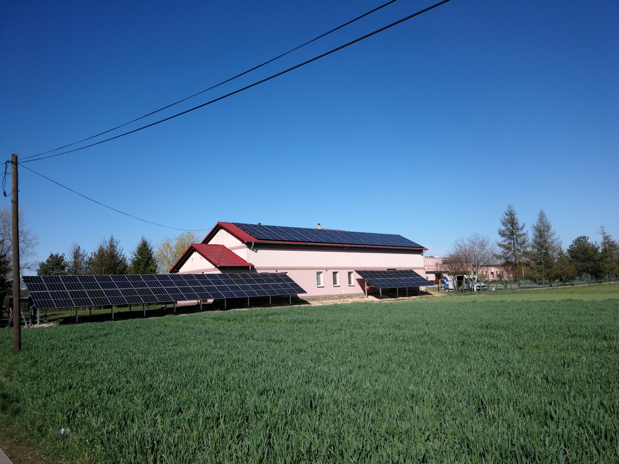 Instalacja paneli słonecznych na dachu i gruncie przy domu jednorodzinnym w słoneczny dzień, widok z pola.