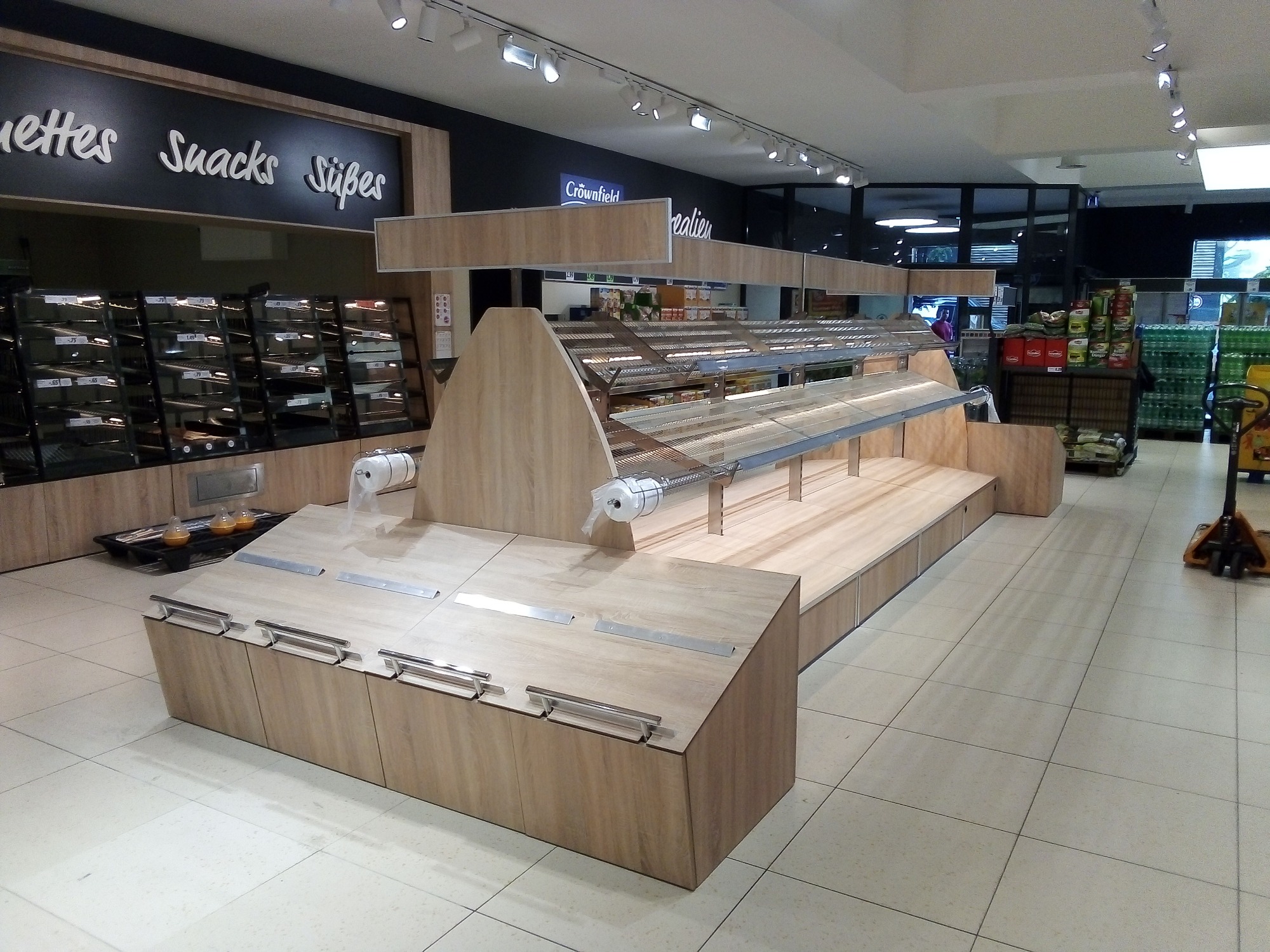 Pusta lada chłodnicza w sklepie spożywczym, z drewnianym wykończeniem i metalowymi uchwytami, podświetlana przez lampy sufitowe.