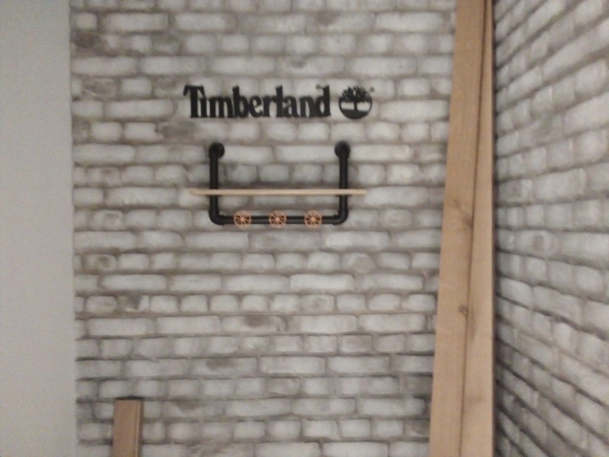 Ściana z cegły z logo Timberland i półką z rur w stylu industrialnym z trzema zaworami.