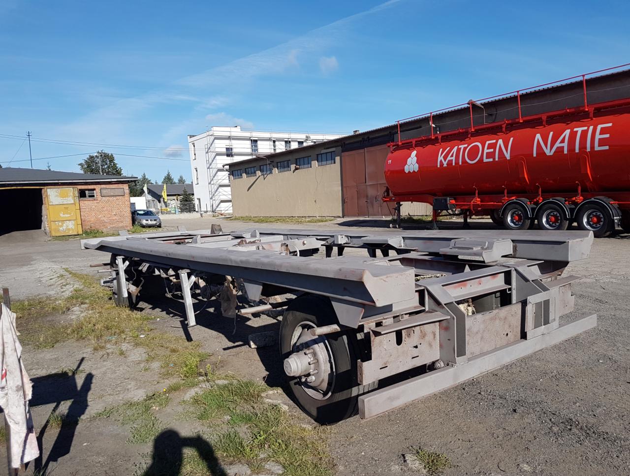 Przygotowana do piaskowania rama naczepy samochodowej na placu, widoczna czerwona cysterna w tle.