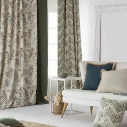 Eleganckie, długie zasłony w botaniczne wzory, z poduszkami dekoracyjnymi i dywanem z juty, w jasnym, minimalistycznym wnętrzu.