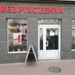 Fasada budynku z czerwonym napisem 'UBEZPIECZENIA' nad witrynami, przed wejściem stoi tablica reklamowa.