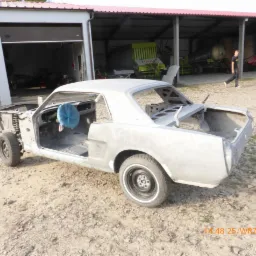 Karoseria klasycznego samochodu w trakcie renowacji, przygotowana do dalszych prac blacharskich i lakierniczych, z widocznym niebieskim pokrowcem na kierownicy i elementami podwozia.