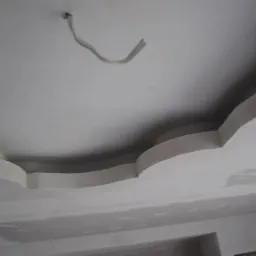 Niedokończony sufit z płyt kartonowo-gipsowych z dekoracyjnymi elementami i wystającym kablem elektrycznym.