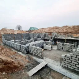 Wznoszenie ścian fundamentowych z bloczków betonowych na placu budowy, widoczne zbrojenia pionowe i podkłady pod kolejne warstwy muru.